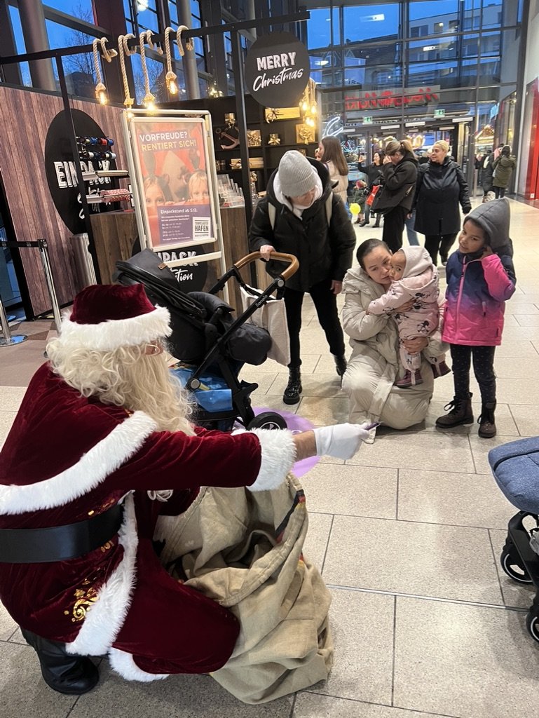 Der Weihnachtsmann kniet vor einer Familie und verteilt Geschenke aus seinem Sack