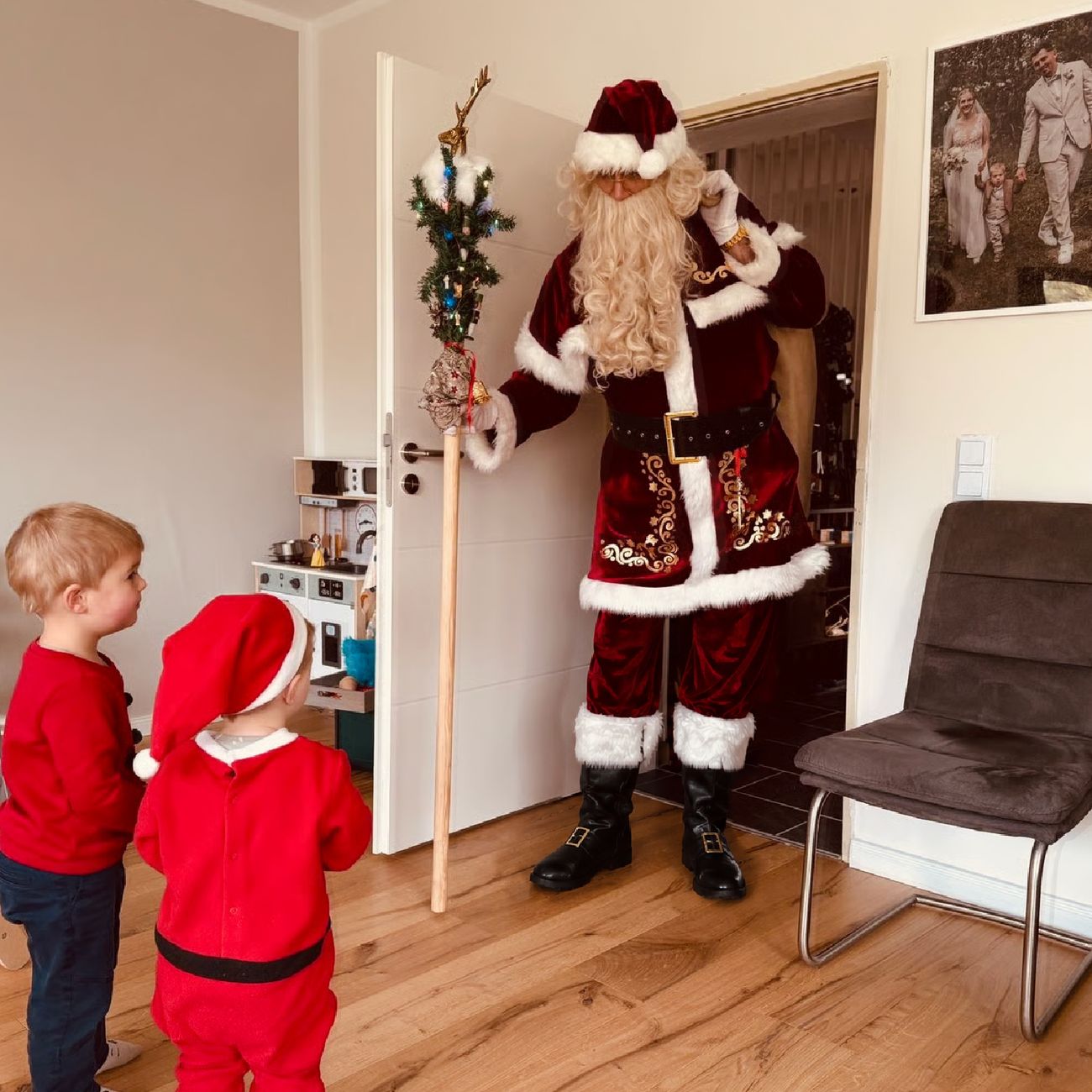Der Weihnachtsmann kommt mit Stab und Sack zur Tür herein, zwei Kinder schauen ihn an