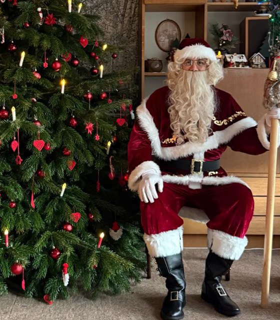 Weihnachtsmann Merlin im vollen Kostüm mit Stab neben dem Weihnachtsbaum