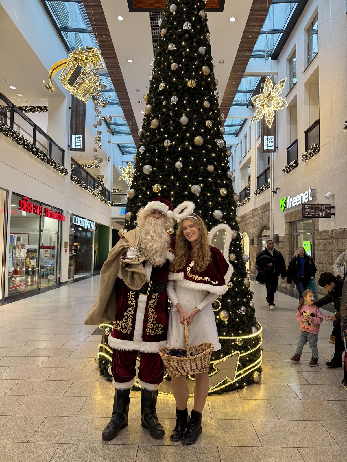 Weihnachtsmann Merlin mit Weihnachtsengel vor dem großen Weihnachtsbaum im Einkaufszentrum